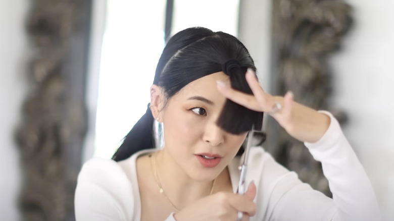 A woman holding hair in front of her face and cutting vertically