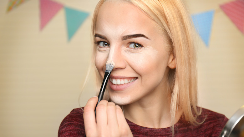 Woman applying highlighter to nose and other parts of face