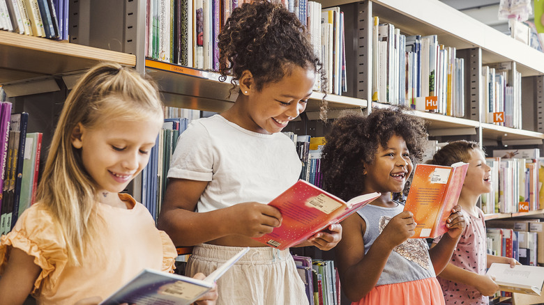 Four children of different ages smiling as they read books in front of a library bookshelf