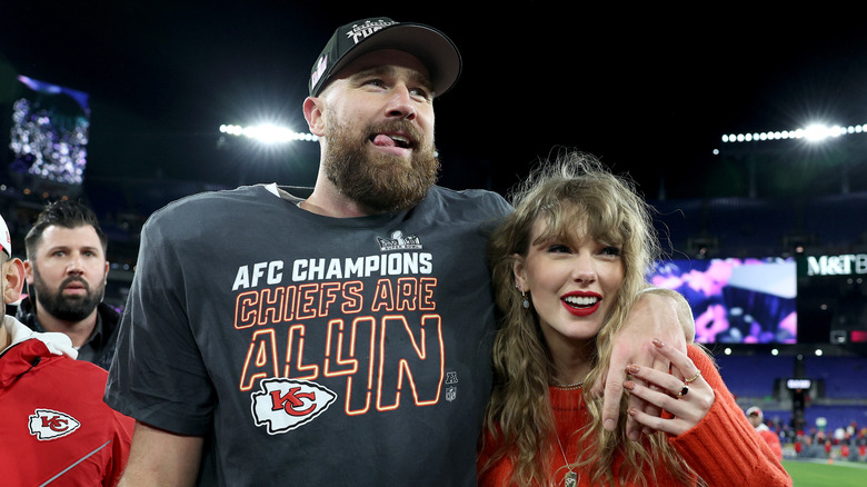 Travis Kelce in a hat and Taylor Swift in a red sweater at an event