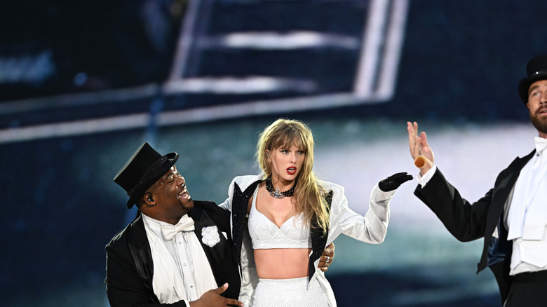 Taylor Swift in a white set and jacket with Travis Kelce in a tuxedo on stage