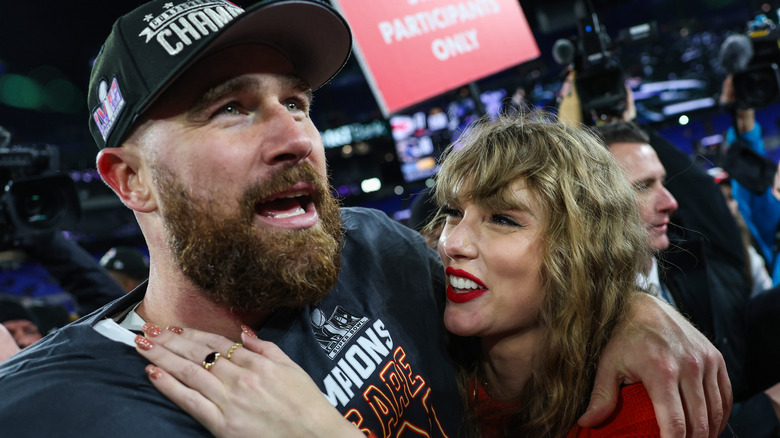 Taylor Swift in a red sweater looking up at Travis Kelce and smiling