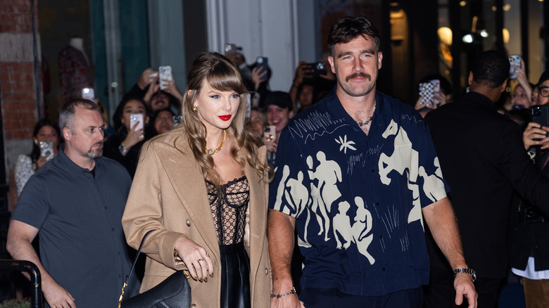 Taylor Swift in a beige coat with Travis Kelce in a blue and cream printed top