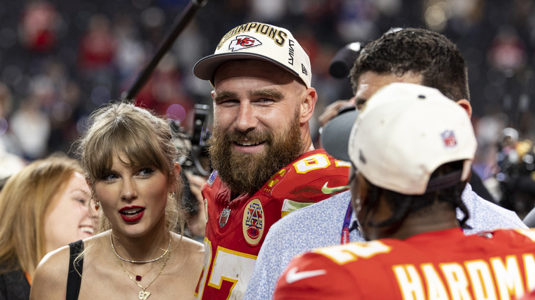 Taylor Swift in a black tank top with Travis Kelce on the sports field