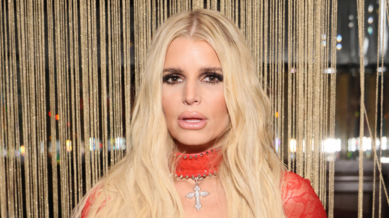 Jessica Simpson in a red, lace dress with a silver cross at an event