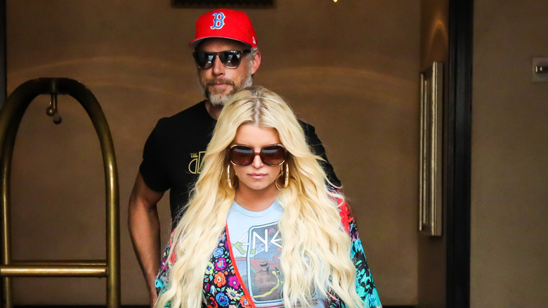 Eric Johnson in a ball cap walking behind Jessica Simpson in big sunglasses