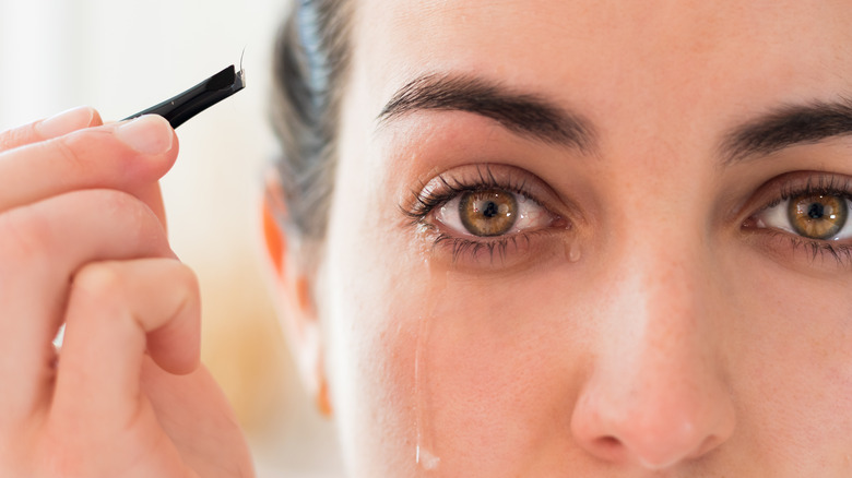 Crying woman using tweezers on eyebrows