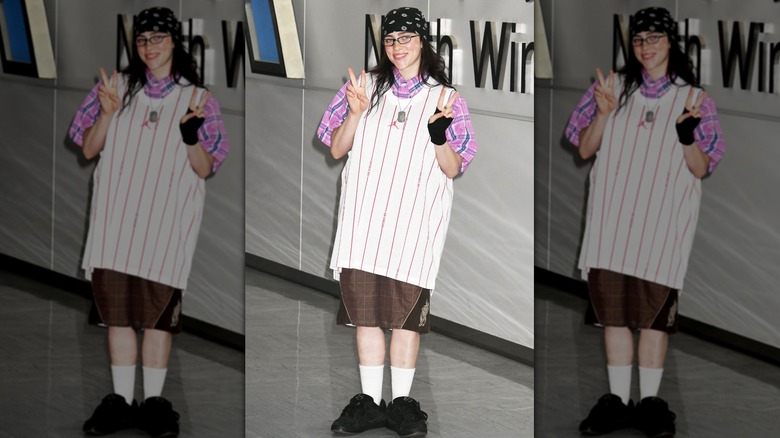 Billie Eilish throwing up two peace signs while wearing a baggy, casual outfit