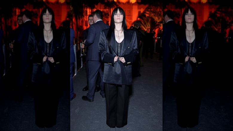 A dark-haired Billie Eilish buttoning her oversized suit jacket at the 2023 Vanity Fair Oscars after party