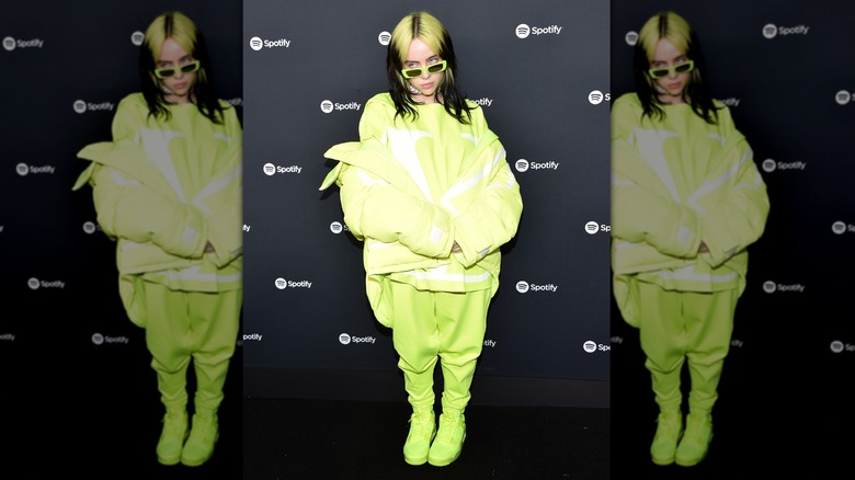 Billie Eilish looking over her neon sunglasses while posing in a monochrome outfit