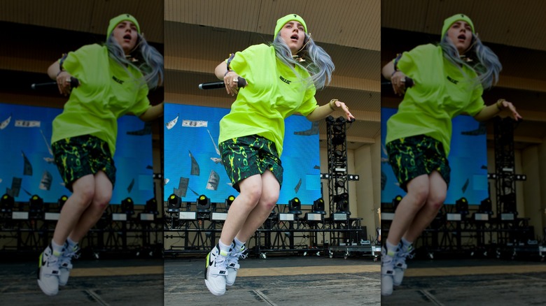 Billie Eilish wearing a bright-colored outfit while jumping during an onstage performance