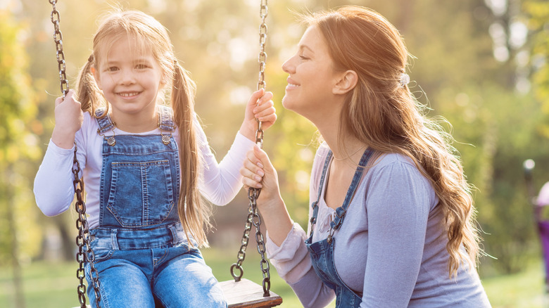 A woman smiling at her daughter on the swing