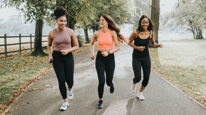 Three smiling women running together outside