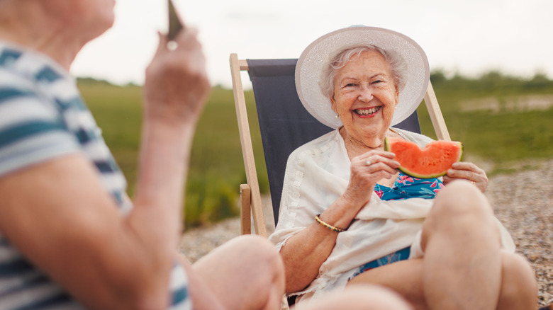 Smiling old woman sitting outside and eating a slice of watermelon