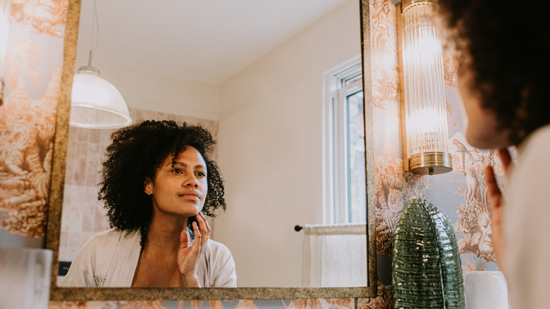 Woman touching her face while looking into a mirror