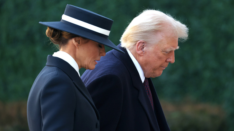 Melania Trump in a blue and white hat and Donald Trump in a suit walking outside