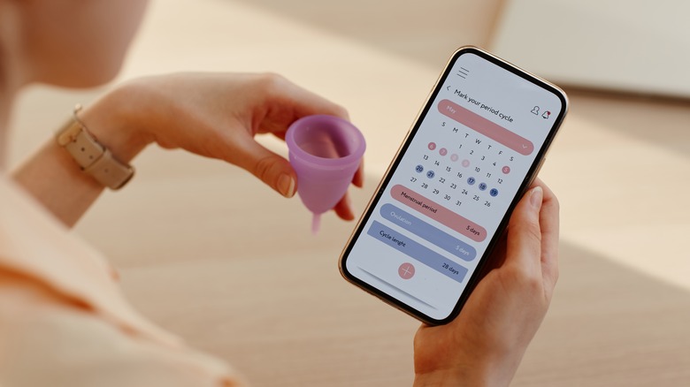 Woman looks at period tracking calendar while holding menstrual cup