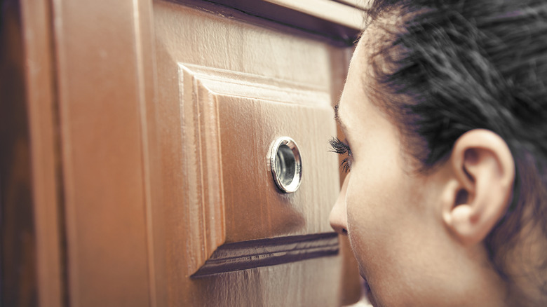 woman looking through a peephole in her door