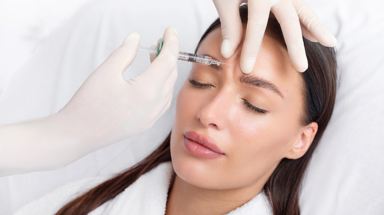 A woman with her eyes closed getting an injection between her eyebrows