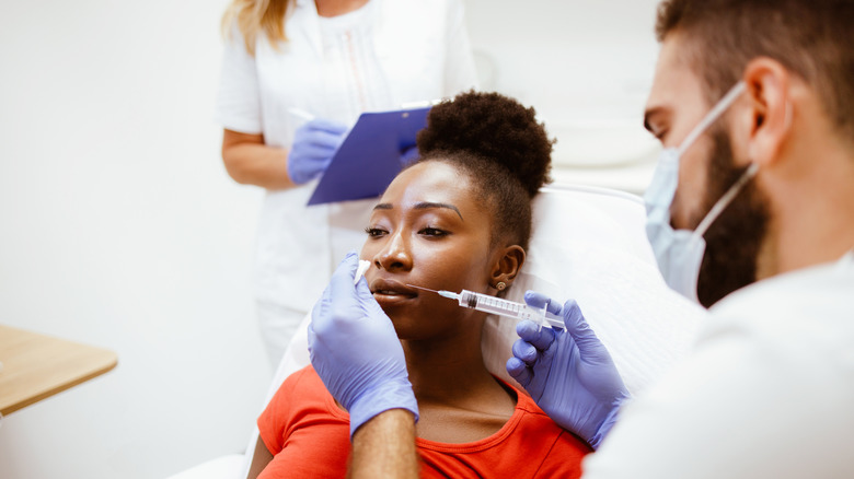 A young woman in a red shirt getting injections in her lips