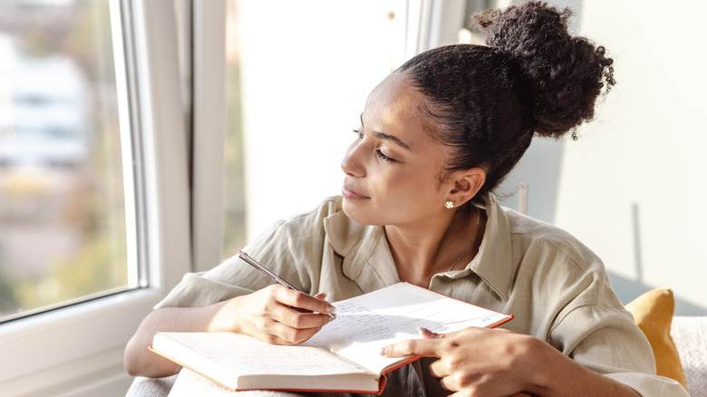 Woman looking out the window while writing in journal