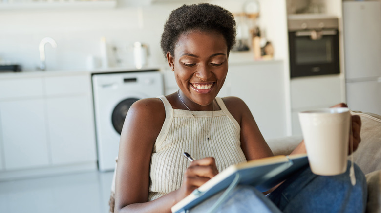 Woman smiling writing in journal with a cup of tea