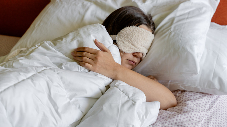 A woman is lying in her bed with an eye mask over her eyes