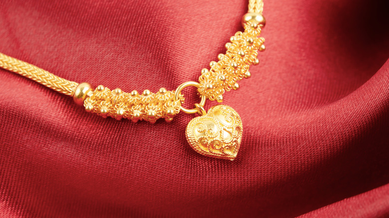 A gold heart shaped pendant laying on red fabric