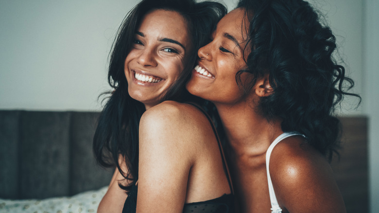 two women smiling and embracing in bed