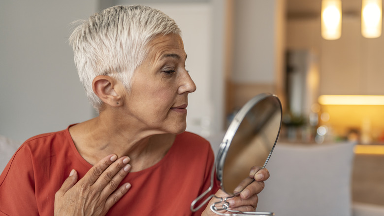 older woman examines reflection in handheld mirror