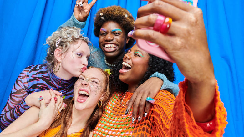 Four, colorfully dressed individuals taking a silly group selfie