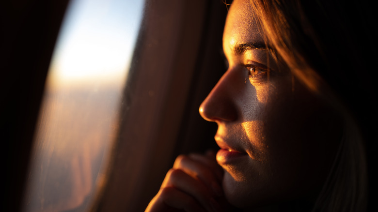 woman looks out window lit by sun