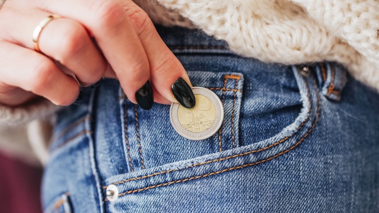 Person holding a coin by their jeans pocket