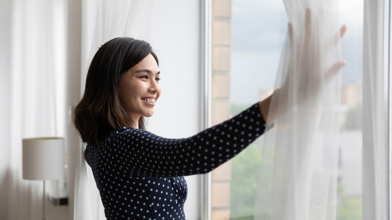 Smiling woman drawing curtains open