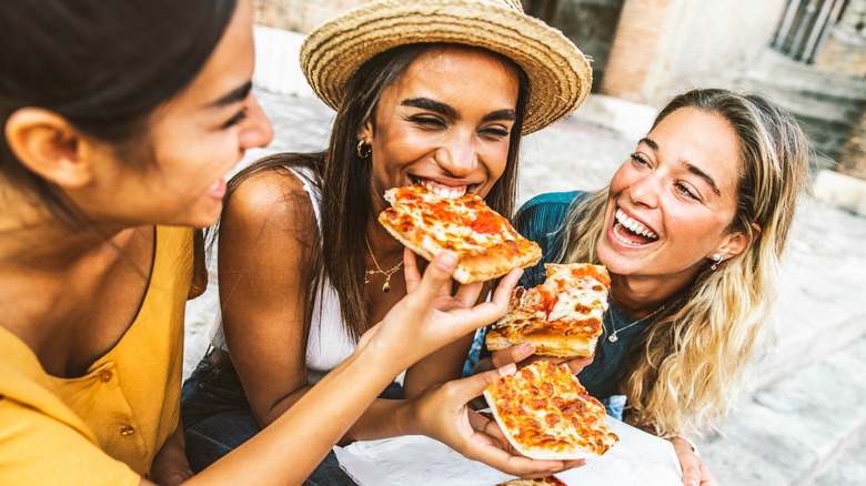 three happy women eating pizza
