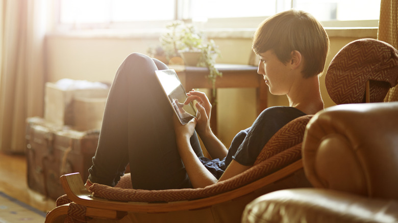 A person sits comfortable in a chair and seems to be reading an e-book