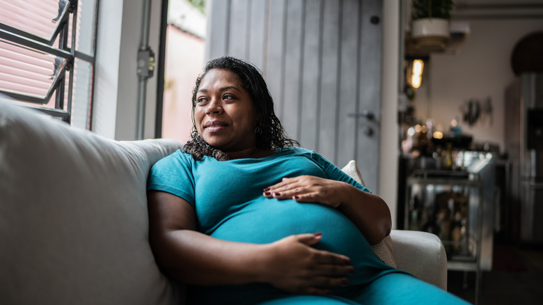 Pregnant woman sits on sofa with hand resting on stomach