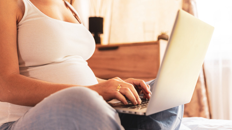 Pregnant woman sits with laptop in her lap