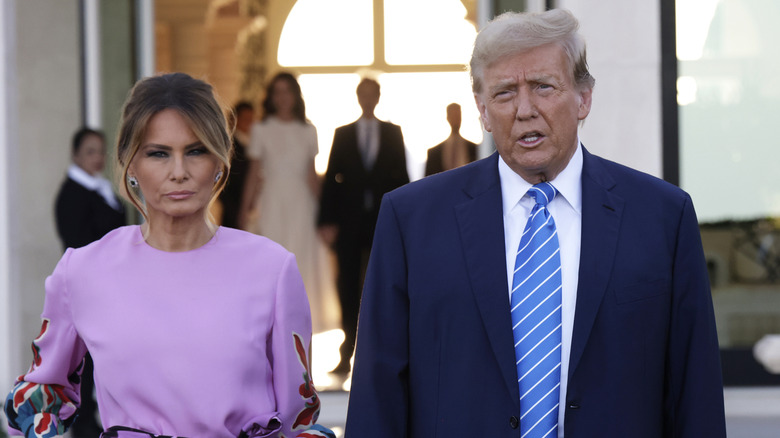 Melania Trump in a purple dress and Donald Trump in a blue suit outside