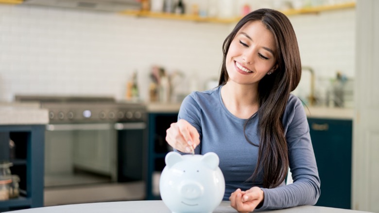 A woman smiles as she puts coins into her piggybank